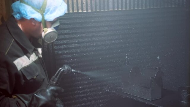 A man in a factory sprays polyurethane on a part. Spraying polyurethane on metal to protect against corrosion and abrasion. Coating with two-component cold curing polyurethanes for industrial products