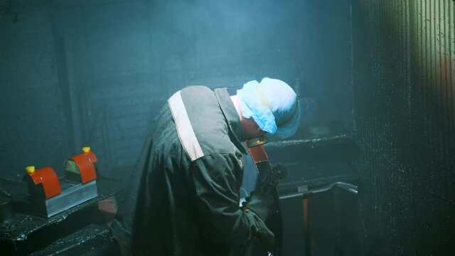 A man in a factory sprays polyurethane on a part. Spraying polyurethane on metal to protect against corrosion and abrasion. Coating with two-component cold curing polyurethanes for industrial products