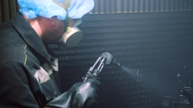 A man in a factory sprays polyurethane on a part. Spraying polyurethane on metal to protect against corrosion and abrasion. Coating with two-component cold curing polyurethanes for industrial products