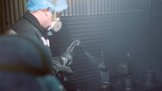 A man in a factory sprays polyurethane on a part. Spraying polyurethane on metal to protect against corrosion and abrasion. Coating with two-component cold curing polyurethanes for industrial products