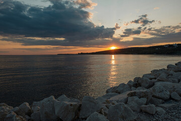 Beautiful sunset over the water overlooking the rocky coastline. The sky flashes brightly as the sun sets over the water.