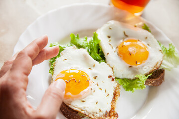 From above anonymous person eating tasty toasts with fried eggs and lettuce for breakfast in morning