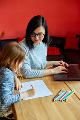 Fototapeta premium Mother working in her home office on a laptop, her daughter sits next to her and draw