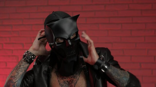 a man in a bdsm demon skull mask, dressed in a leather cloak with leather bracelets and straps on his body