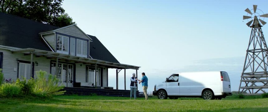 HANDHELD WIDE Adult Mature Caucasian female signing documents with handyman general worker in front of her house. White car with copy space. Shot with 2x anamorphic lens