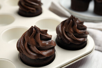 Delicious chocolate cupcakes with cream in baking tray on white wooden table, closeup