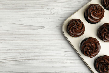 Delicious chocolate cupcakes with cream in baking tray on white wooden table, top view. Space for text