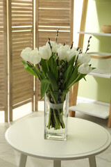 Beautiful bouquet of willow branches and tulips in vase on table indoors