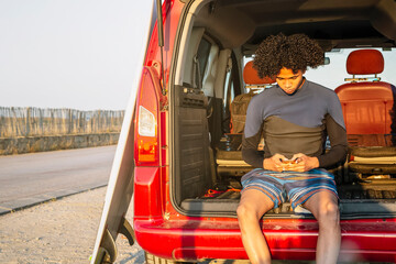 Young Latino surfer with afro hair talks on a mobile phone in the caravan