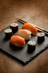 mixed sushi with chopstick over black stone on wood background