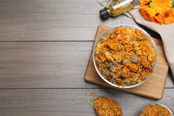 Dry calendula flowers and bottle with tincture on wooden table, flat lay. Space for text