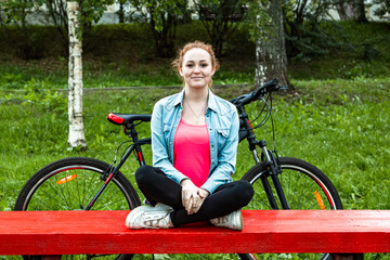 Obraz premium A cheerful girl with a bicycle sits on a park bench.