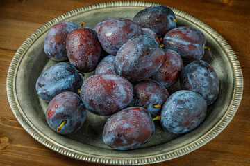 fresh plums on a plate on wooden table