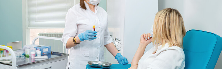 Fototapeta premium unrecognizable laboratory technician holds blood tube and patient with a bent arm sits on a chair.