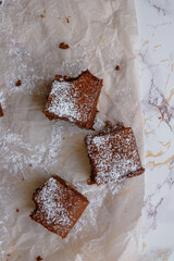 Three brownie squares dusted with powdered sugar on a piece of baking parchment. Flatlay. Light background.