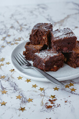 Brownie squares dusted with powdered sugar with a fork on a white plate. Light background. 