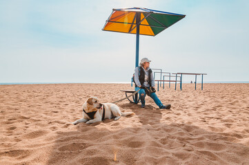 A tourist girl is resting with a dog under a chaise longue on an empty lonely beach