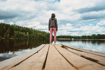 The view from below from the wooden pier of the forest lake to the girl standing alone with her back