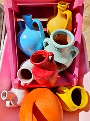 Several colorful jugs in a wheelbarrow. The jugs are made of clay and painted in vibrant colors.