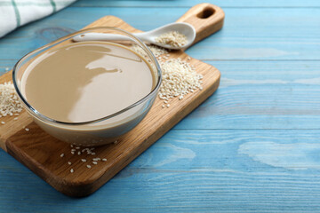 Tasty sesame paste and seeds on light blue wooden table, space for text