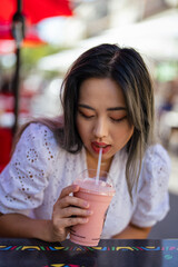 Young Petite Asian Woman Drinking a Strawberry and Banana Smoothie