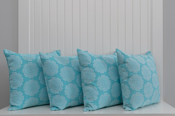 Photograph of a set of four teal throw pillows standing on a shelf in a home