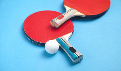 Table tennis rackets and a white plastic ball on a blue background.