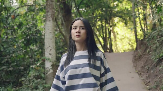 young adult asian woman walking alone inside the forest, hiking trekking in the national park, human and nature, outdoor activity pursuit, tropical woods, walking toward camera on the waling path