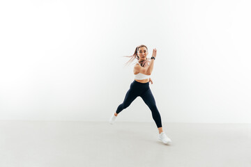 Young sportswoman running forward indoors. Muscular female exercising against a white wall.