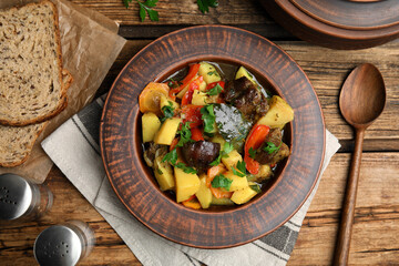 Tasty cooked dish with potatoes in earthenware served on wooden table, flat lay