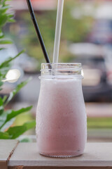 Milk shake, smoothie, in a glass mug or bottle with two straws on wooden handrail, street in the background