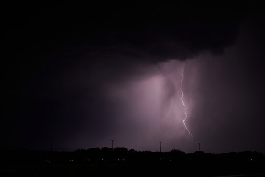 Gewitter. Blitz in der Nacht erhellt Wolken, Silhouette einer Stadt hebt sich ab.