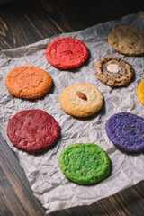 Various colored cookies on baking parchment and wooden table
