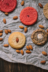 Various cookies surrounded by almonds  on baking parchment and wooden table. Flatlay