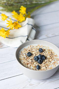 Granola, yogurt, blueberries in white bowl. Yellow flowers on background. Vegan diet.
Healthy breakfast. Close up photo. Selective focus on bluberries.