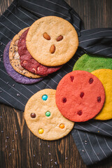 Various large colored cookies on black lined kitchen towel and wooden table