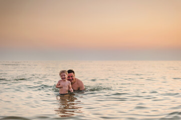 dad and son have fun swimming in the sea at sunset in the summer
