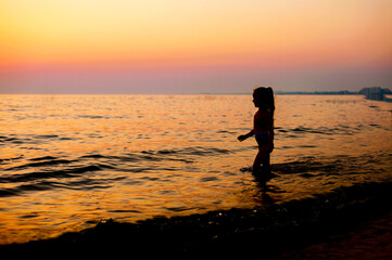 silhouette of a little girl in a swimsuit at sunset standing in the sea