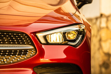 headlight and radiator grille of a beautiful red car with yellow tint