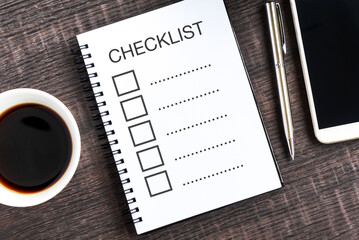 Checklist on note pad with smart phone, cup of coffee and pen