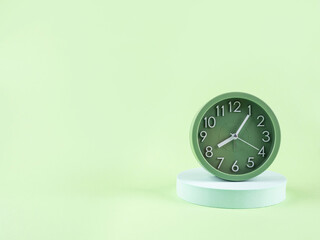 Green alarm clock on turquoise podium on green background