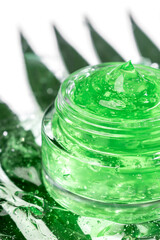 Cosmetic products for skin care and makeup. Transparent green moisturizer aloe vera gel in jar, face serum with bubble on white background with green leaves. Vertical.