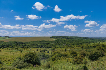 Sunny rural Russian landscape with green fields and sparsely wooded areas. Beautiful landscape with fields and green vegetation under a blue sky with white cumulus clouds in the countryside of Adygea.