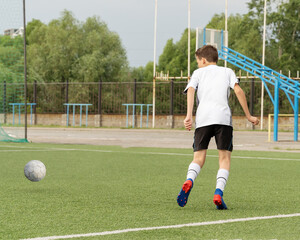 The boy loves to play football, trains with the ball on the artificial turf and scores a goal. The boy plays football