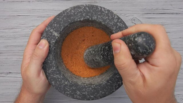 Top view of male hands with a pestle mixing finely grounded spices in the mortar