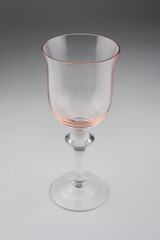 a single, empty wine glass made of pink tinted glass on a soft gray background with copy space