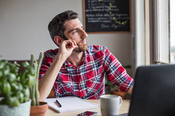 Man thinking and looking out of window whilst working at home