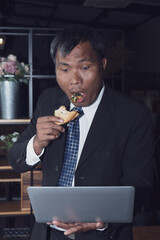 An Asian Businessman is busy with his work while eating a pizza food in the work place office but he is happy with that hard work