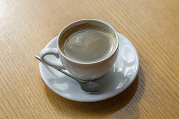 White porcelain coffee cup with saucer and spoon on wooden table in cafe