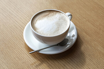 White porcelain coffee cup with saucer and spoon on wooden table in cafe
